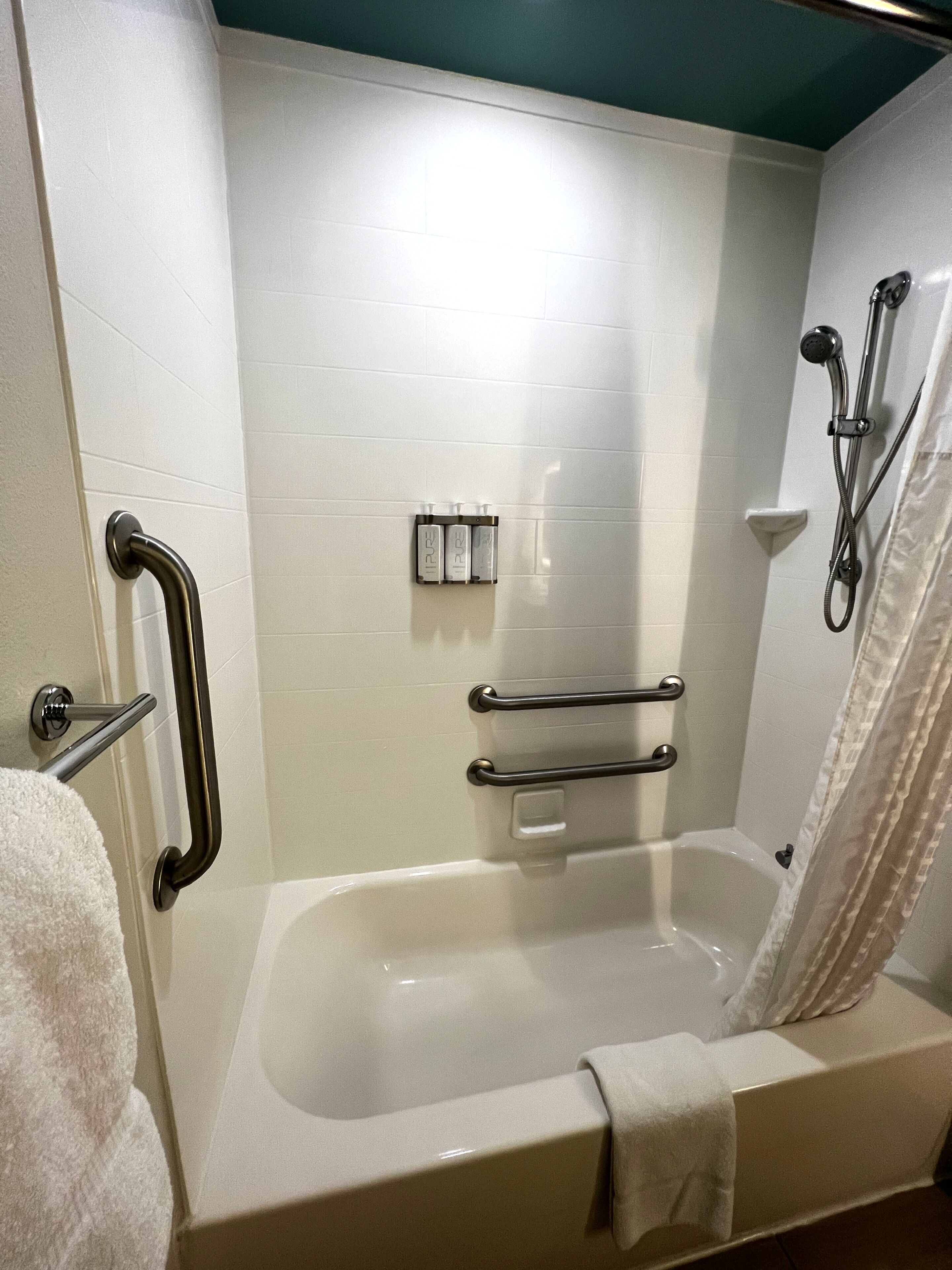 A bathroom with a bathtub, grab bars, a shower head, and a towel rack.