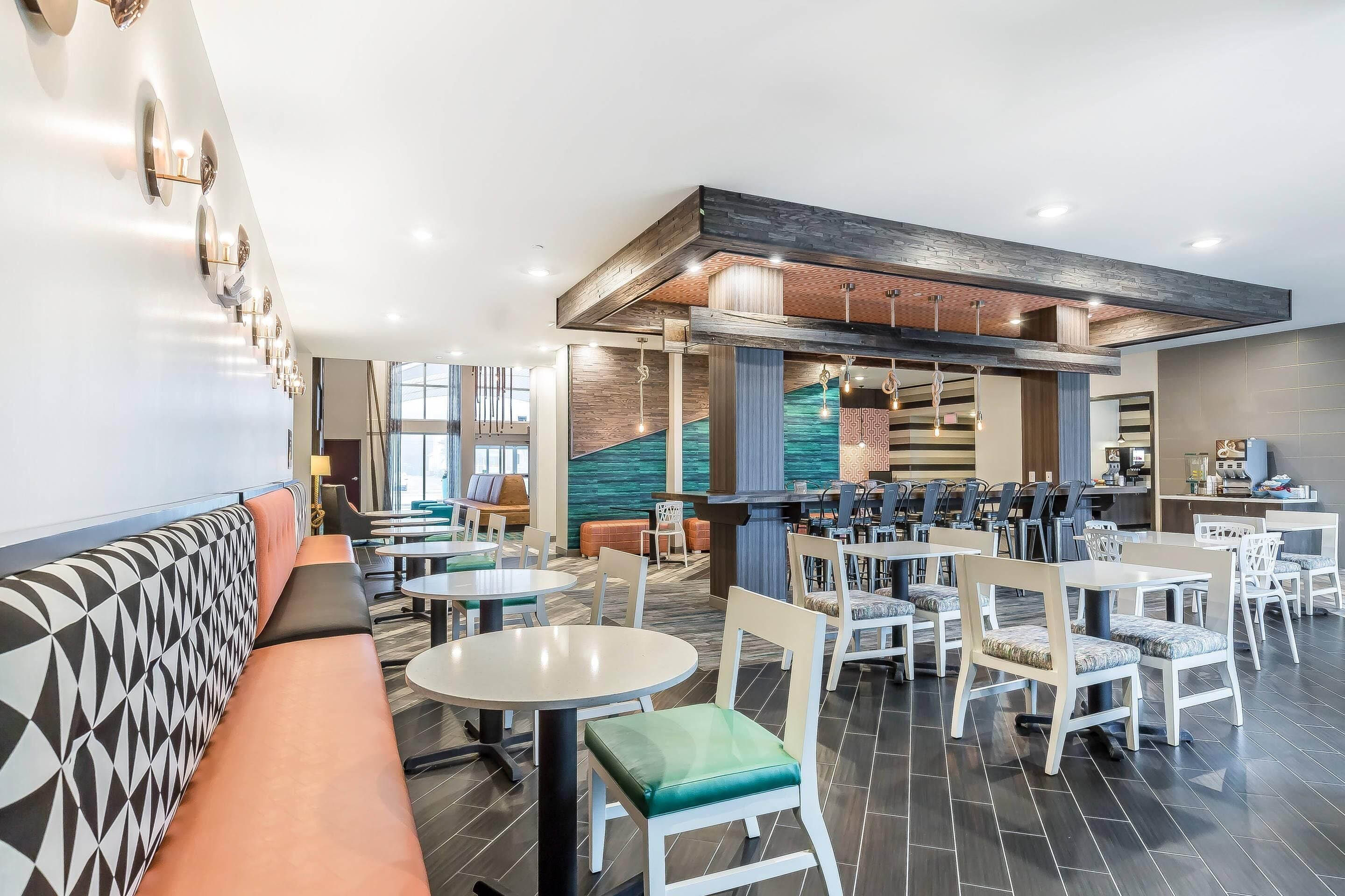 Een modern restaurant met een lange balie, meerdere tafels en een bankgedeelte met een patroon.