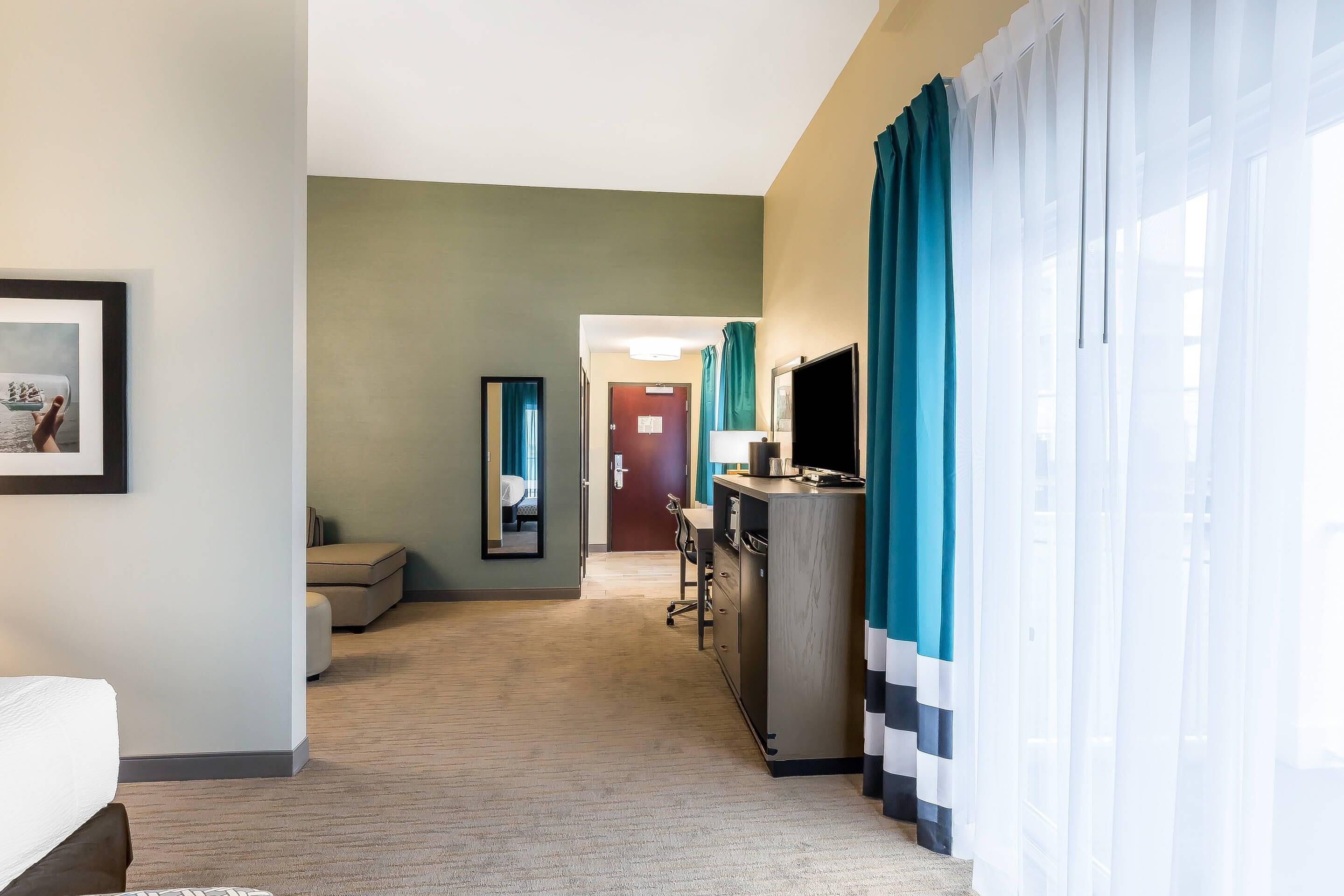Une chambre d’hôtel avec un lit, un bureau avec un ordinateur, une télévision et une fenêtre avec des rideaux.