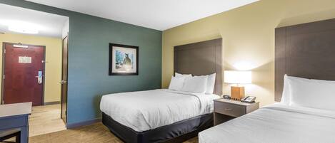 A hotel room with two beds, a desk, a chair, a door, and a framed picture on the wall.
