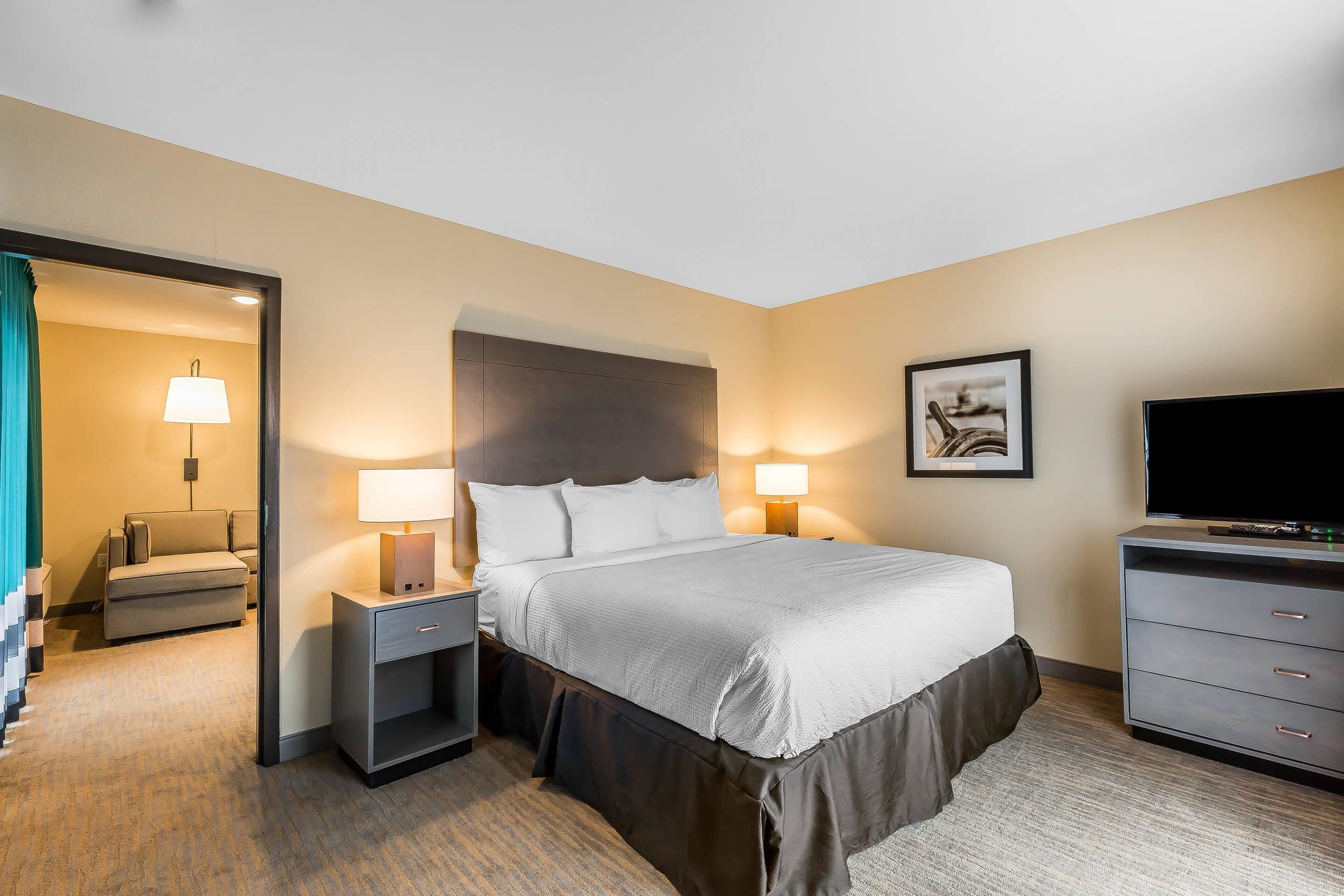 A hotel room with a bed, bedside lamps, a TV, a desk, and a chair.