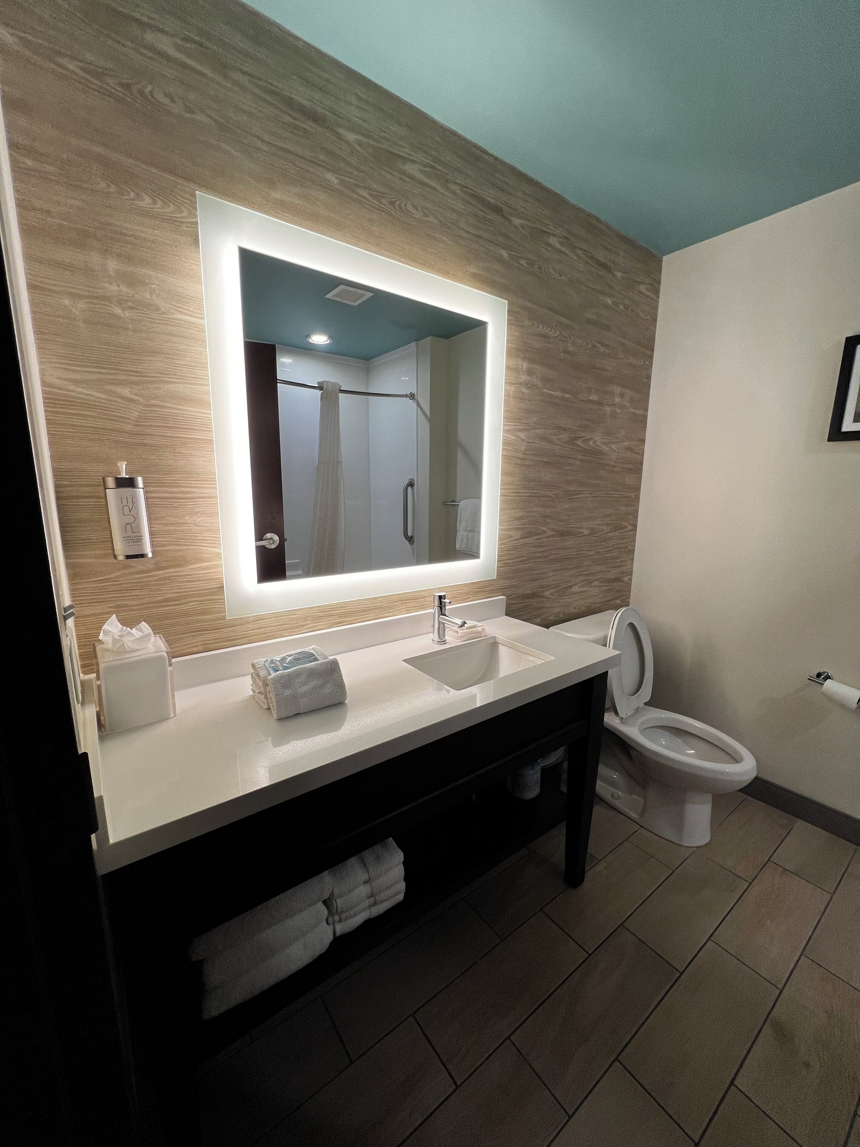 A modern bathroom with a large mirror, a sink, a toilet, and a towel rack.