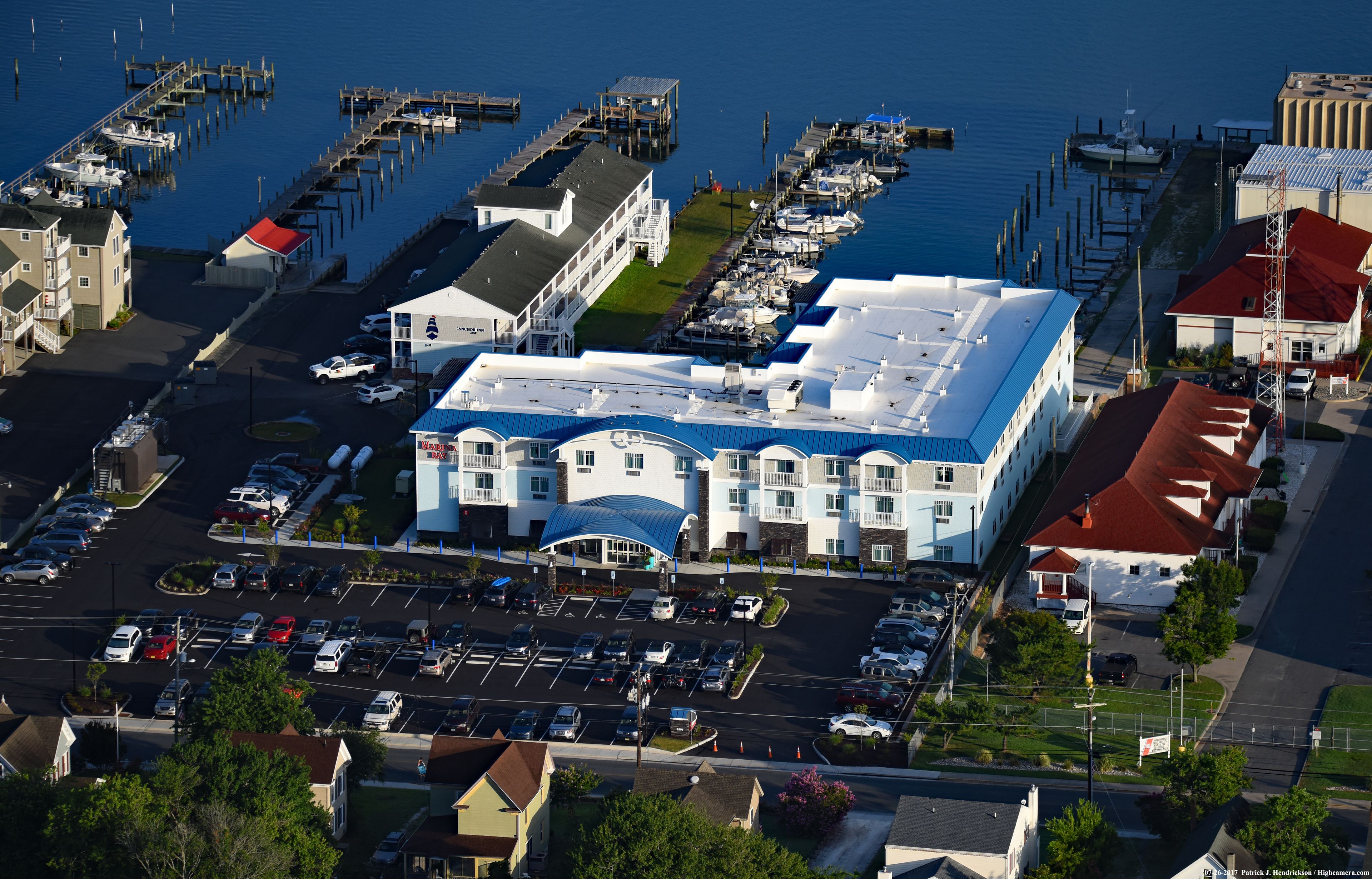 Vue aérienne d’une marina avec des bateaux amarrés, d’un grand bâtiment doté d’un toit bleu et d’un parking.