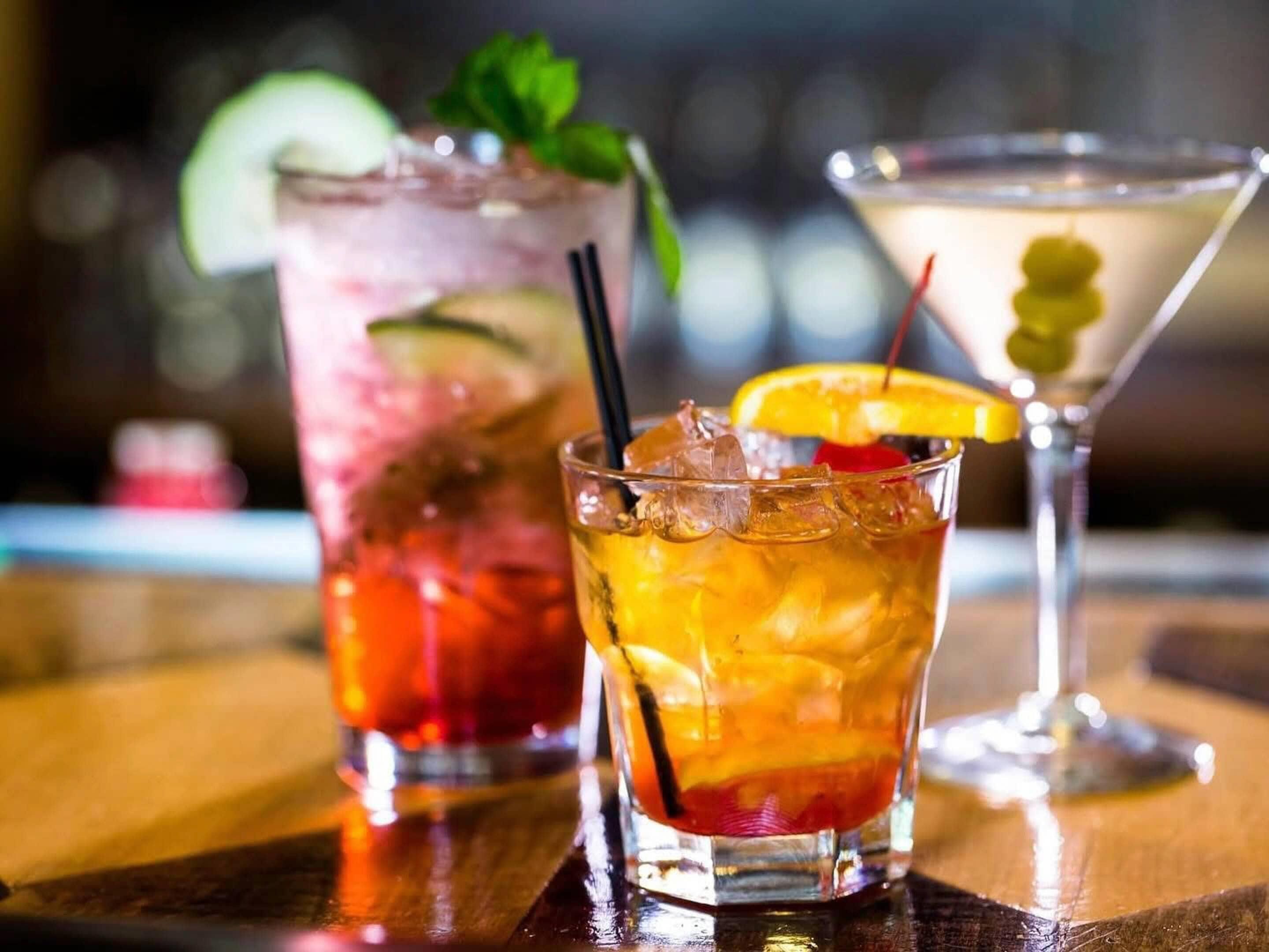 Three different cocktails in glasses on a wooden table.