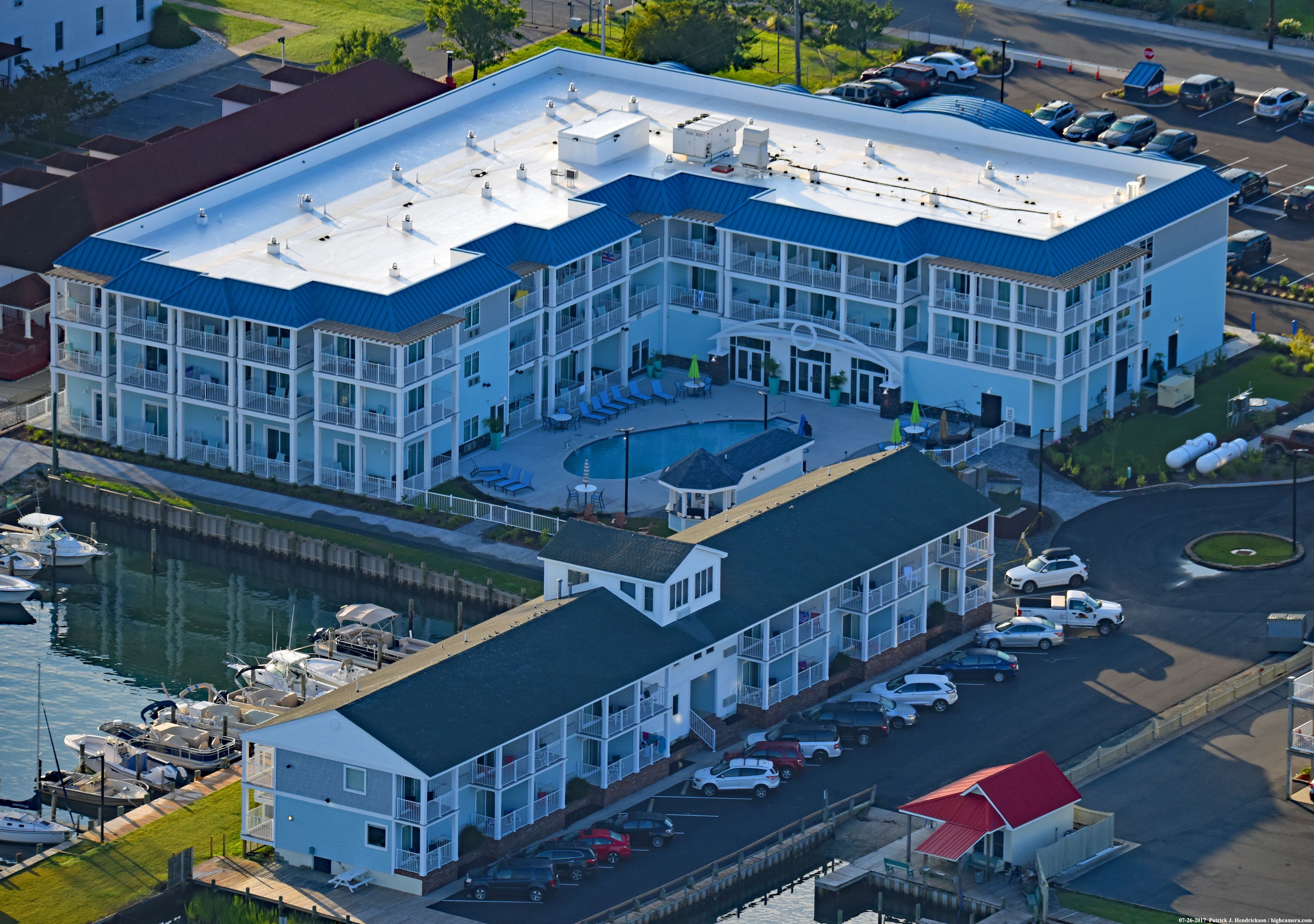 A multi-story hotel with a rooftop pool, a marina with boats, and a parking lot.