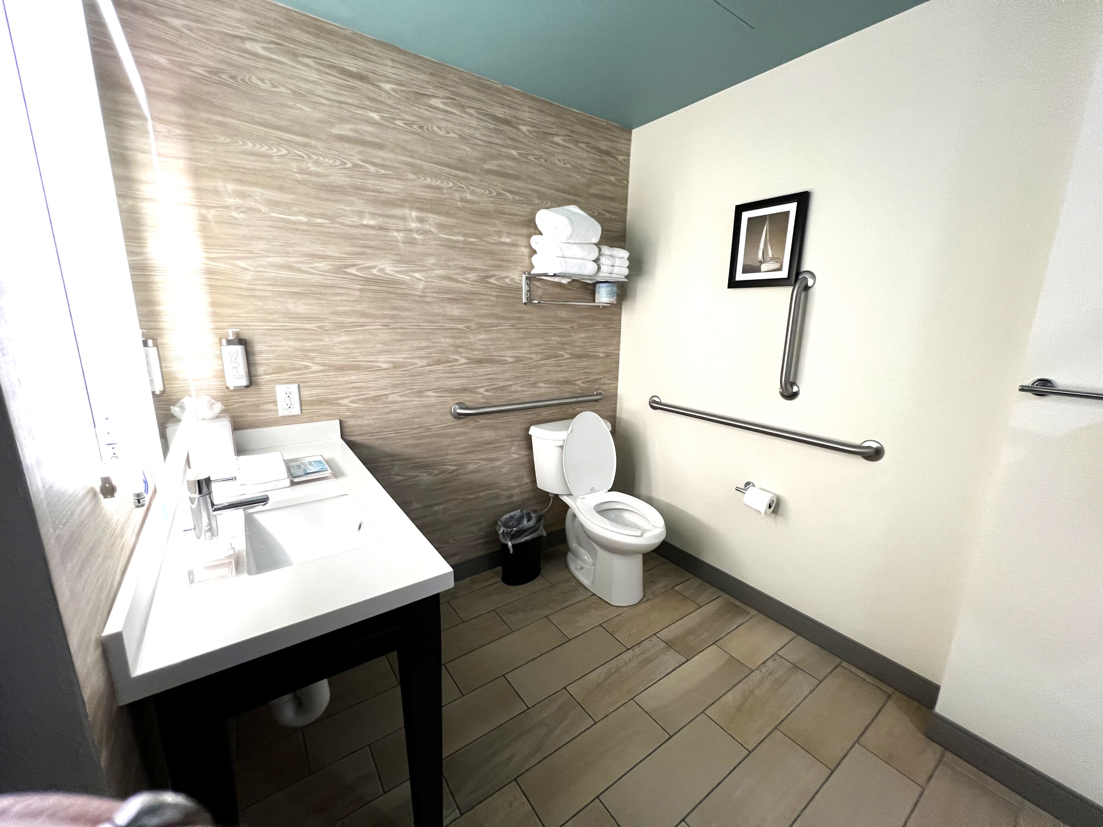 Un baño moderno con lavamanos, inodoro y barras de apoyo.