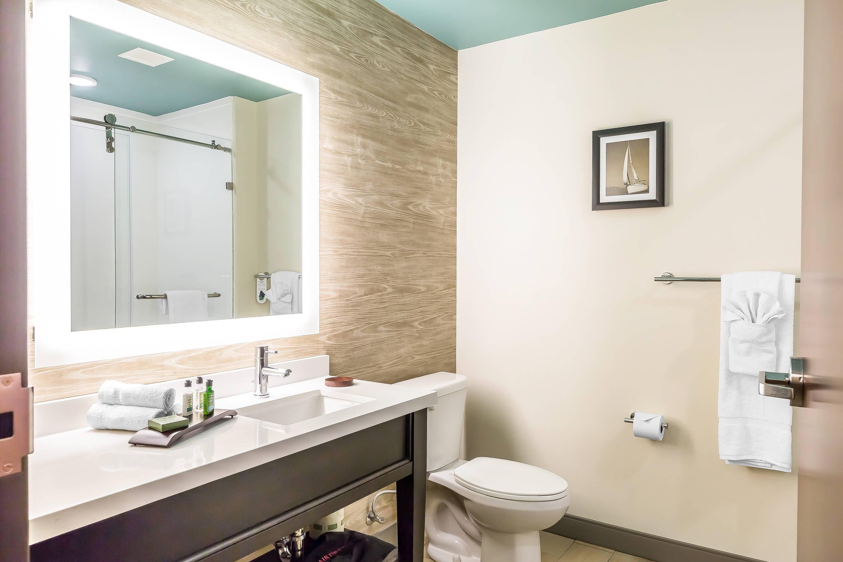 A modern bathroom with a large mirror, white sink, and a toilet.