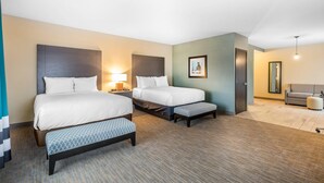 A hotel room with two beds, a bench, a nightstand with a lamp, a framed picture on the wall, and a sofa in the corner.