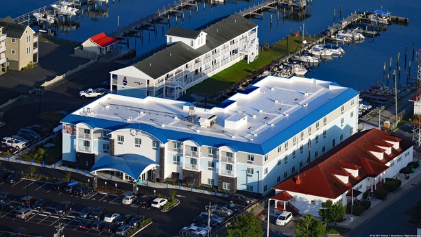 Een meerhoog hotel met een blauw dak, gelegen nabij een jachthaven met aangemeerde boten.