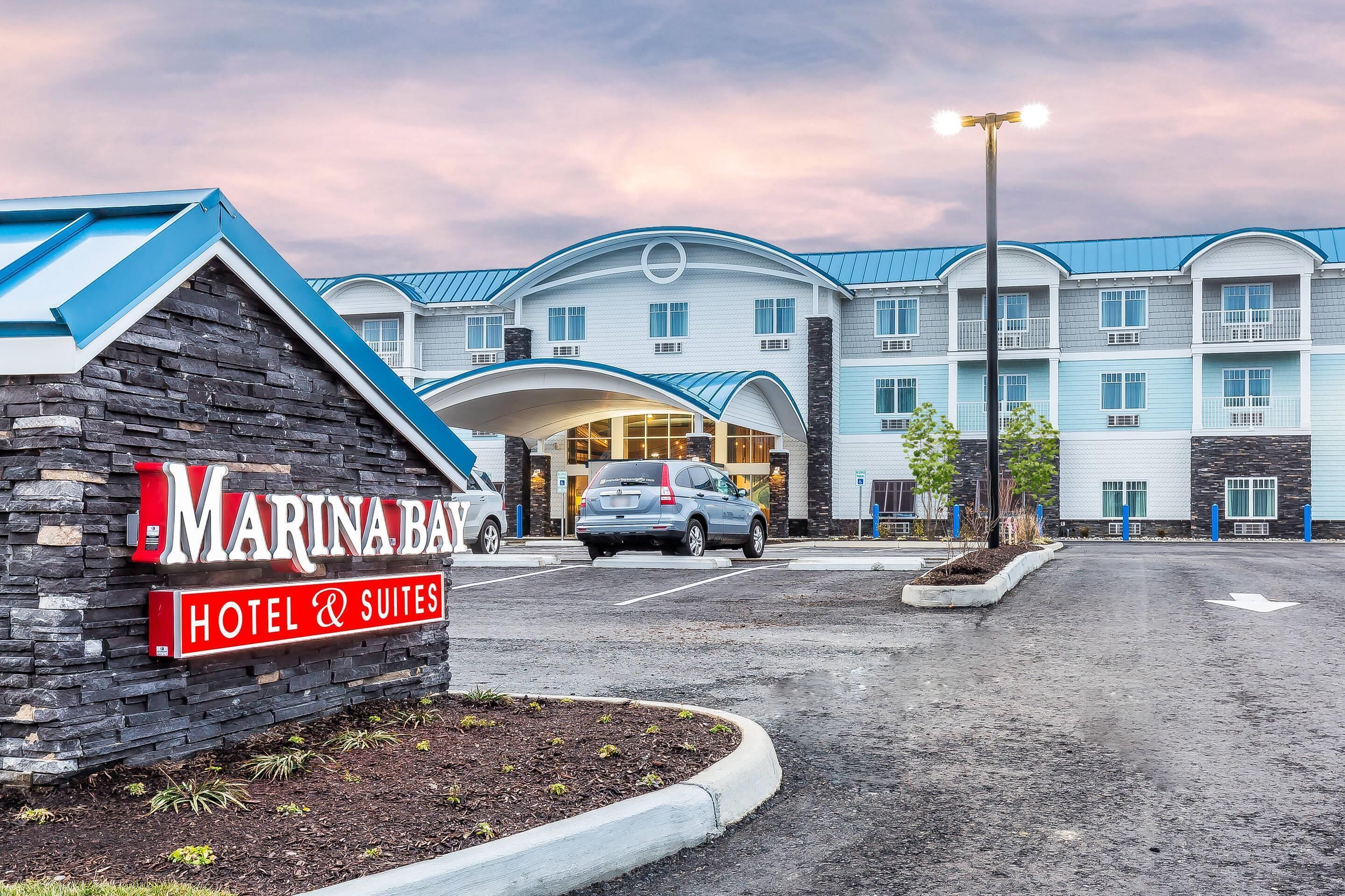 A hotel with a sign reading 'MARINA BAR HOTEL & SUITES' and a parking lot with a car.