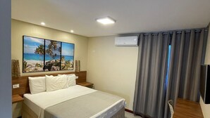 A hotel room with a large bed, a desk, and a painting of a beach scene. - Pousada Le Baron (Marechal Deodoro)