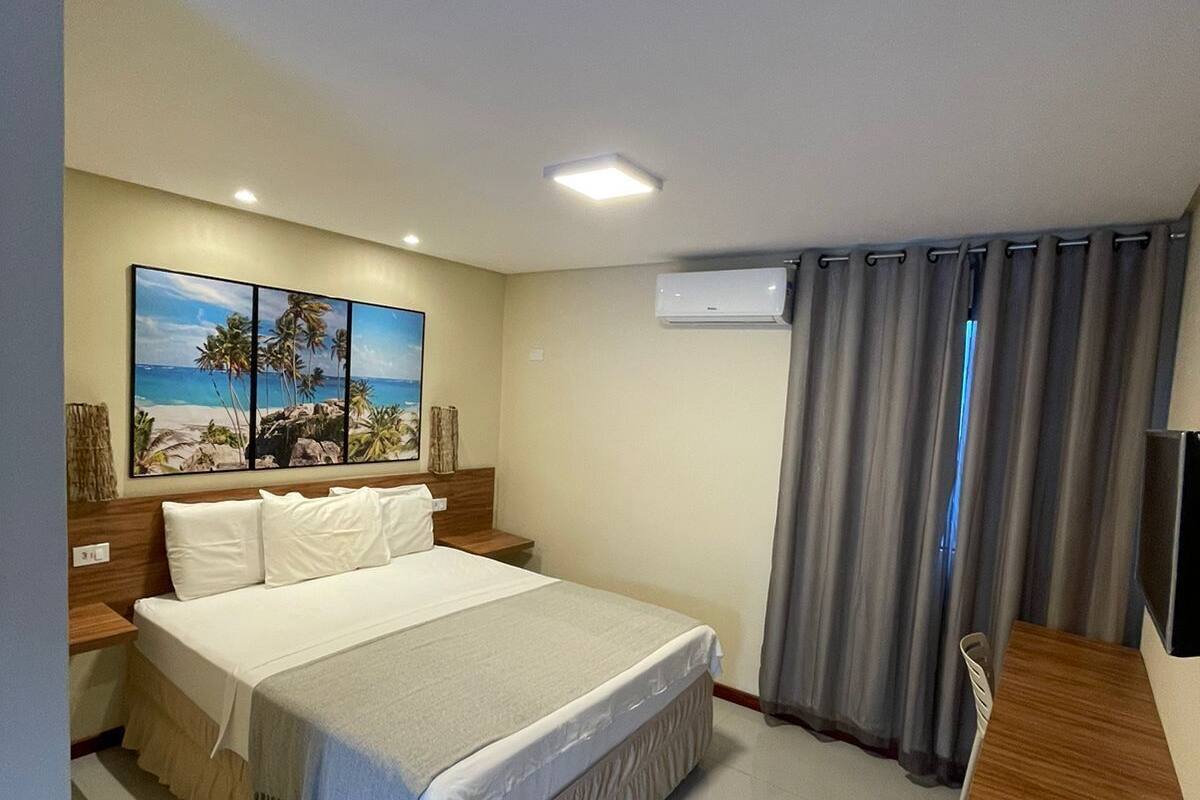 Ett hotellrum med en stor säng, ett skrivbord och en tavla som föreställer en strandvy.