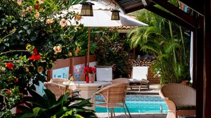 A poolside area with wicker furniture, a tiled pool, and lush greenery. - Pousada Le Baron (Marechal Deodoro)