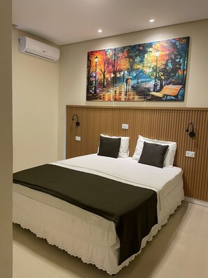 Habitación de hotel con una cama grande, un cuadro en la pared y un equipo de aire acondicionado.