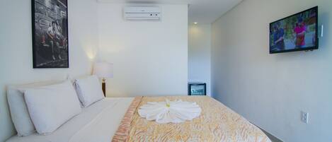 A hotel room with a neatly made bed, a wall-mounted air conditioner, a television on the wall, and a framed picture above the bed.