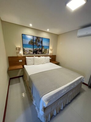 Un dormitorio con cama, mesitas de noche, aire acondicionado de pared y un cuadro con temática marina.