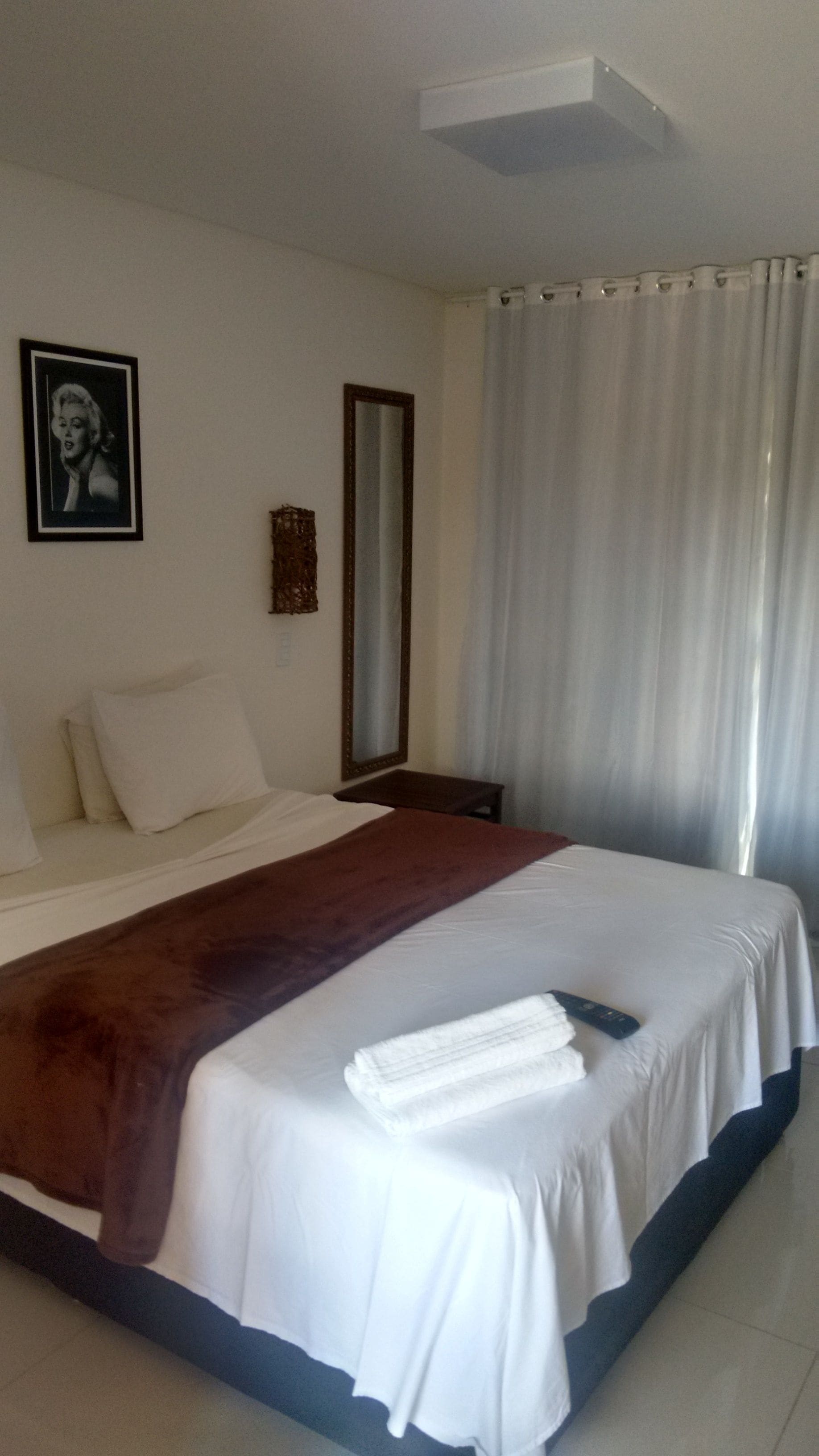 A hotel room with a large bed, a mirror, a picture on the wall, and a window with curtains.
