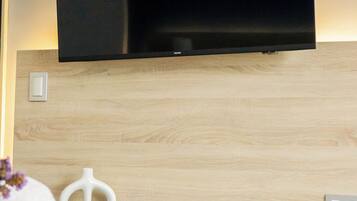 Habitación de hotel moderna con un televisor de pantalla plana montado en una pared de madera, un florero blanco, una pequeña mesa con un control remoto y un letrero que indica prohibido fumar.