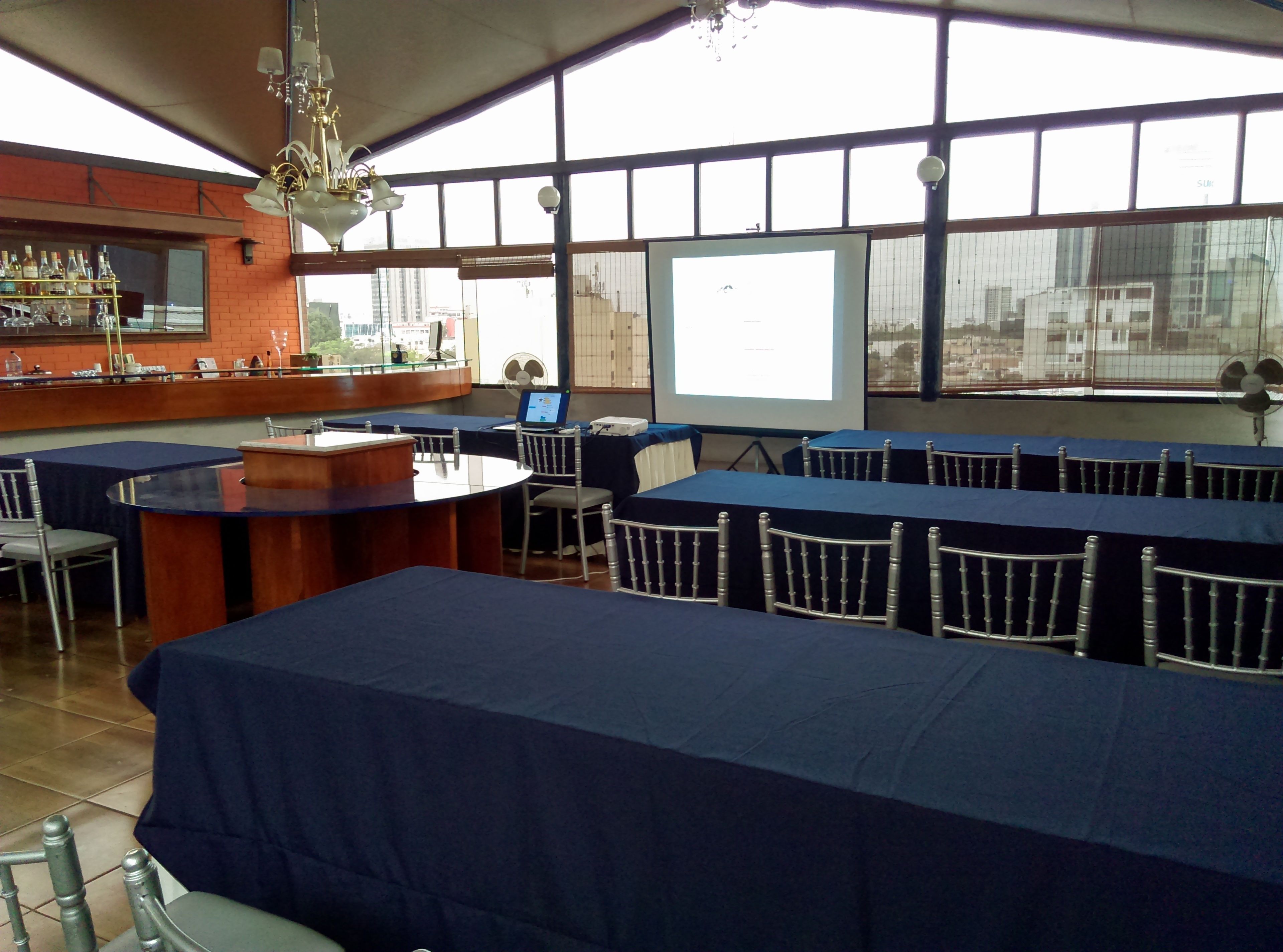 A conference room with a large screen, tables with chairs, a bar area, and a chandelier.