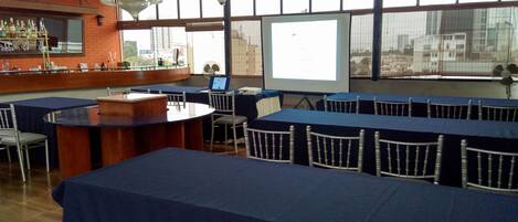A conference room with a large screen, tables with chairs, a bar area, and a chandelier.