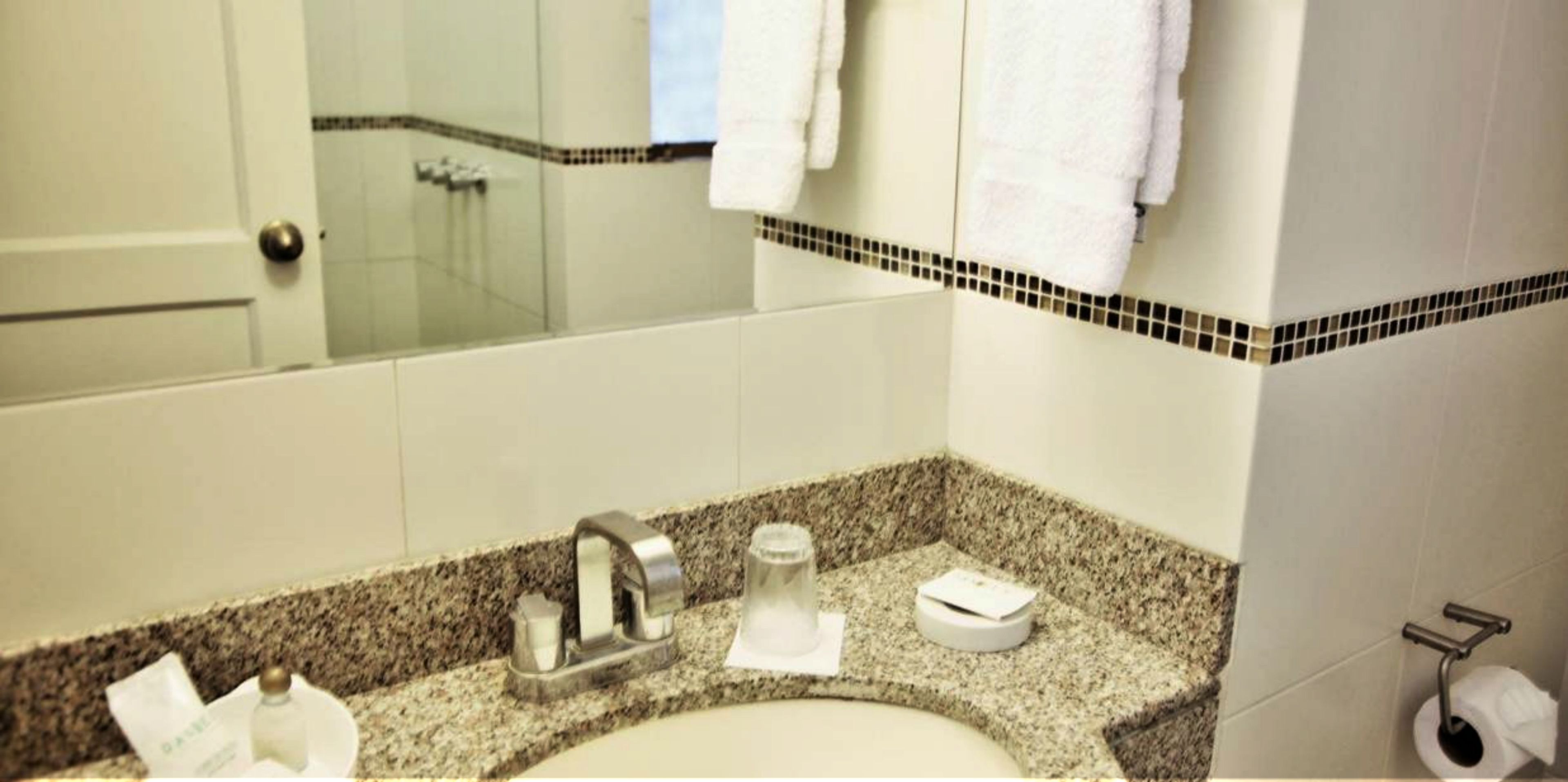 A bathroom with a granite countertop, a sink, a mirror, a shower, and a towel rack.