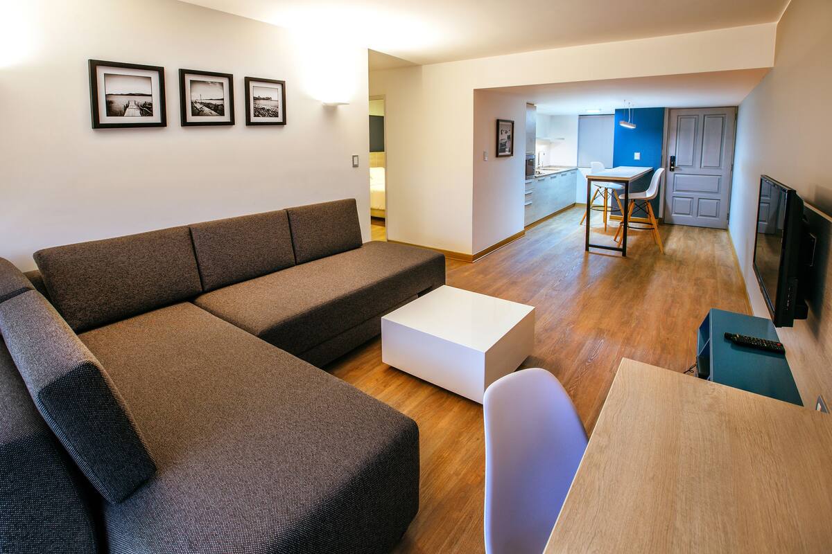 A modern living room with a sectional sofa, a white coffee table, and a dining area with a small table and chairs.