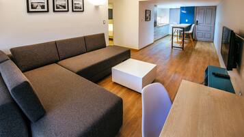 A modern living room with a sectional sofa, a white coffee table, and a dining area with a small table and chairs.