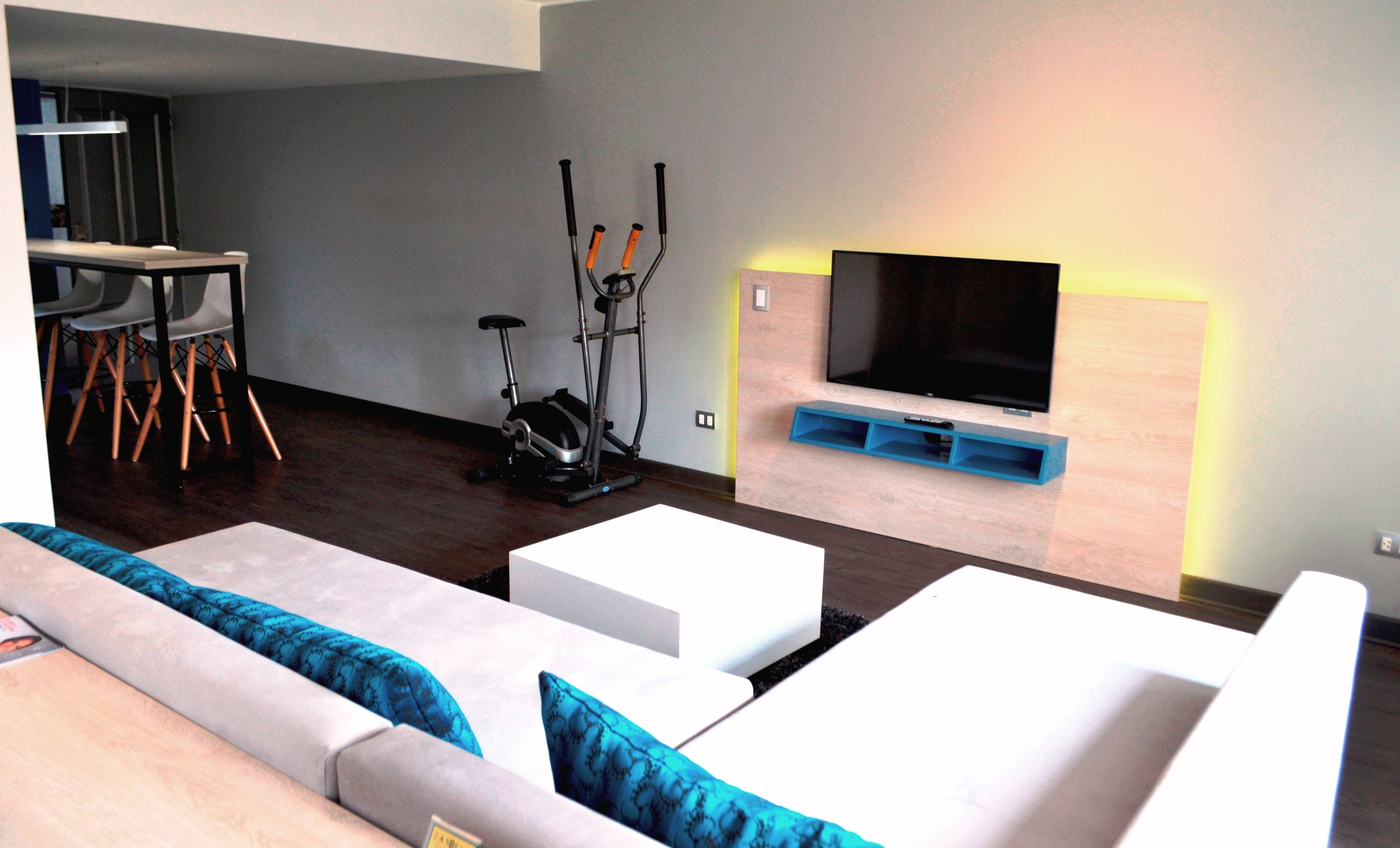 A modern living room with a sofa, a TV mounted on a wooden wall, and exercise equipment.