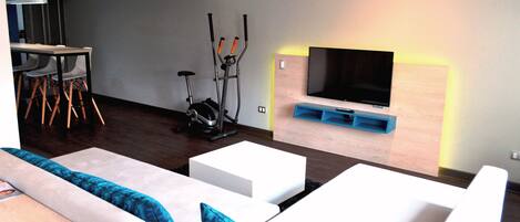 A modern living room with a sofa, a TV mounted on a wooden wall, and exercise equipment.