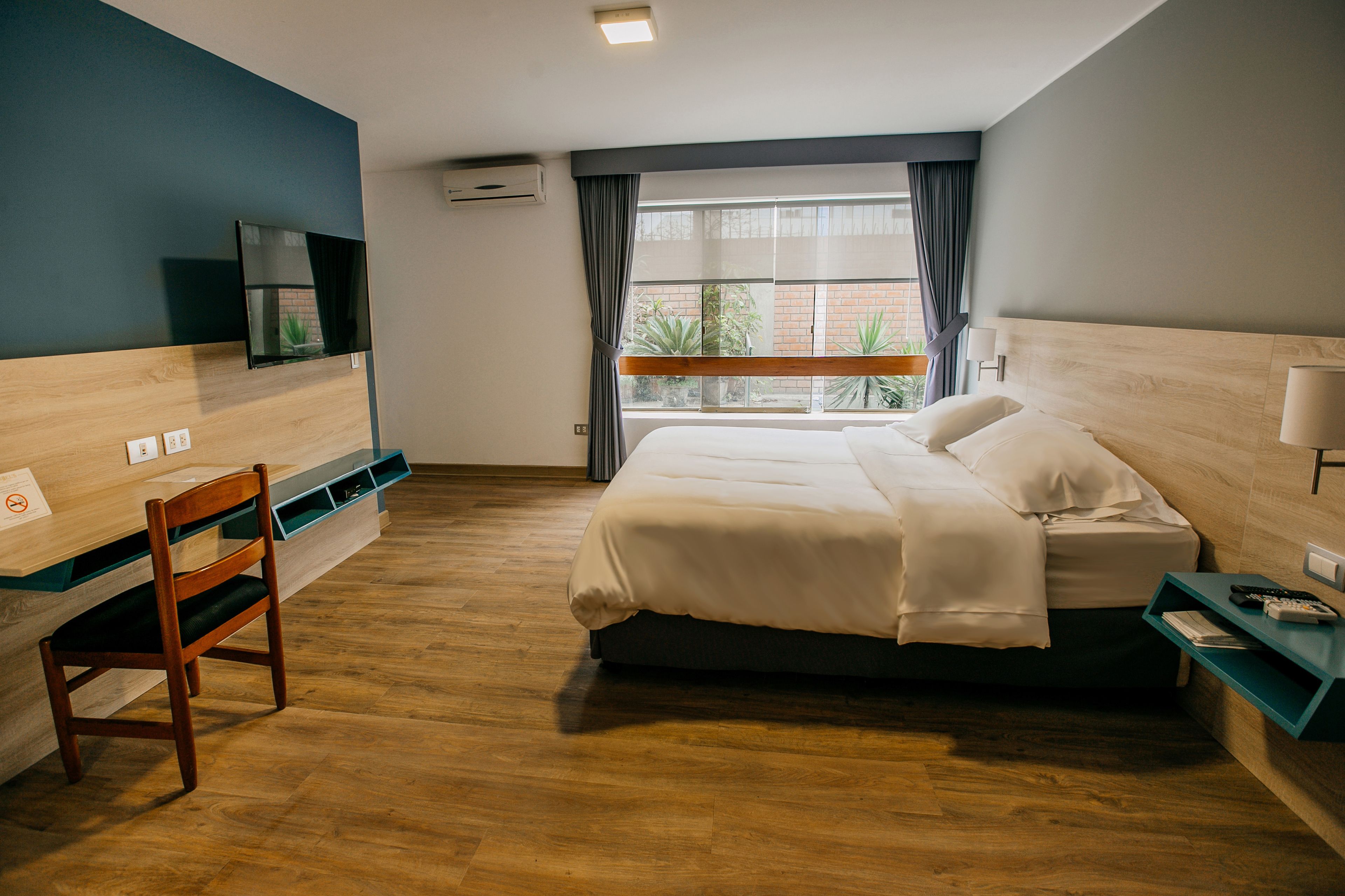 Habitación de hotel con cama, escritorio, silla, televisión y ventana con cortinas.