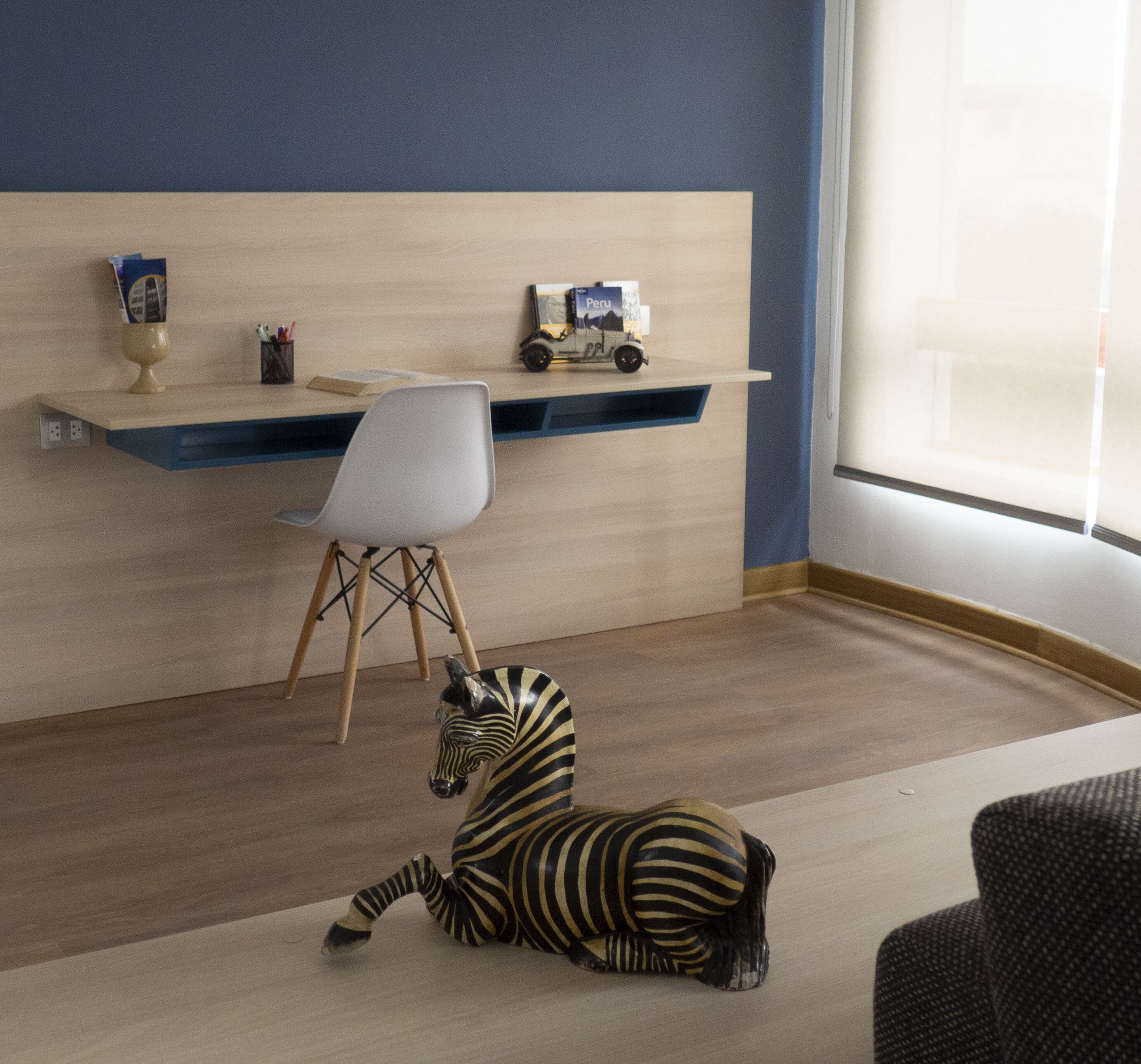 Una habitación con escritorio, silla y un juguete de cebra en el suelo.
