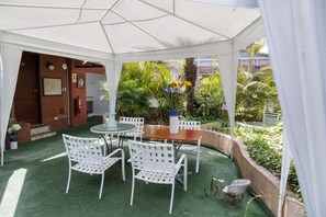 A covered patio with a table and chairs, surrounded by greenery and a brick wall. - Daniel's Apart Hotel (Lima)