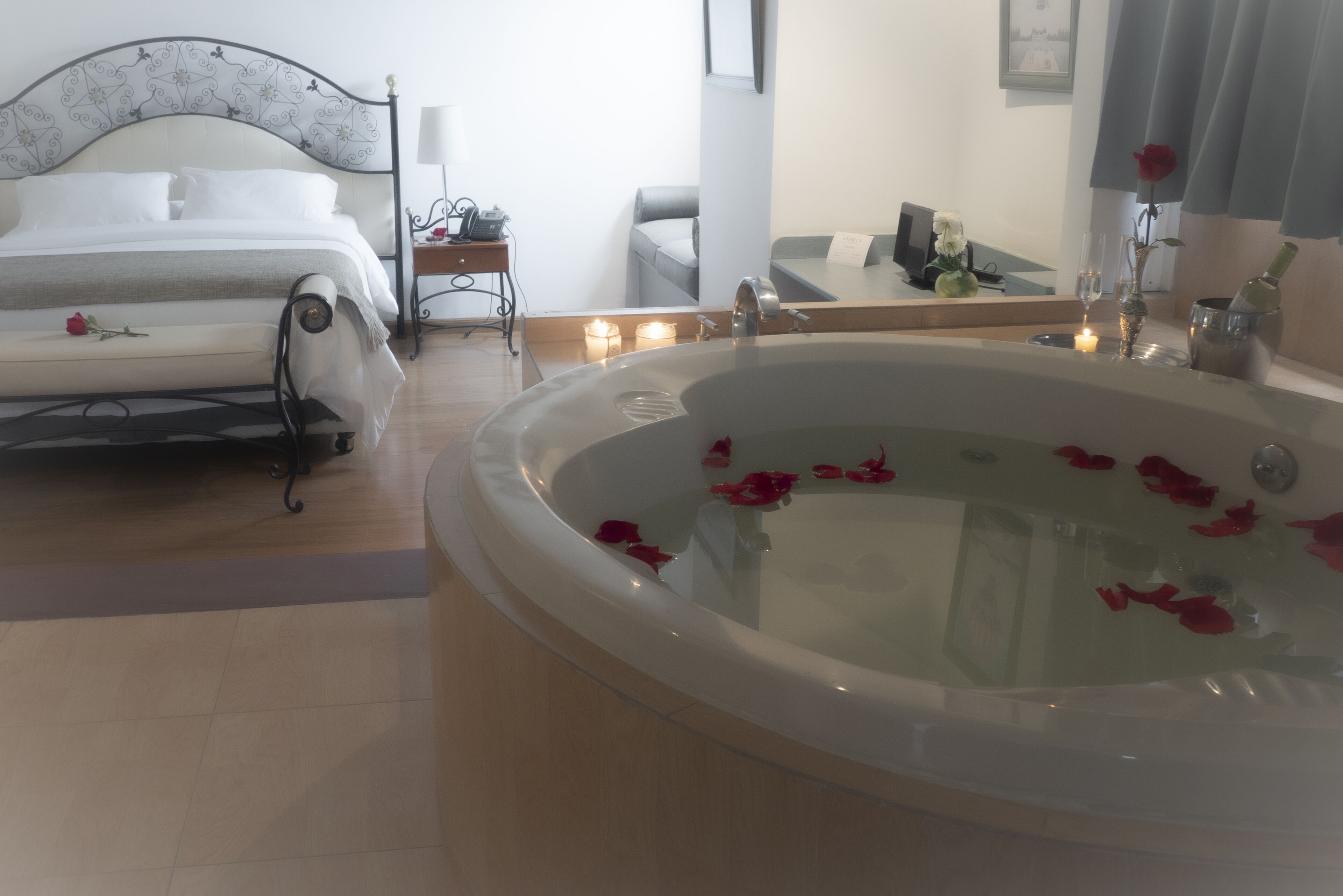 Un dormitorio con cama, una mesita de noche, un espejo y una bañera grande llena de pétalos de rosa.
