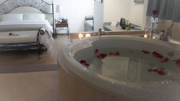 Un dormitorio con cama, una mesita de noche, un espejo y una bañera grande llena de pétalos de rosa.