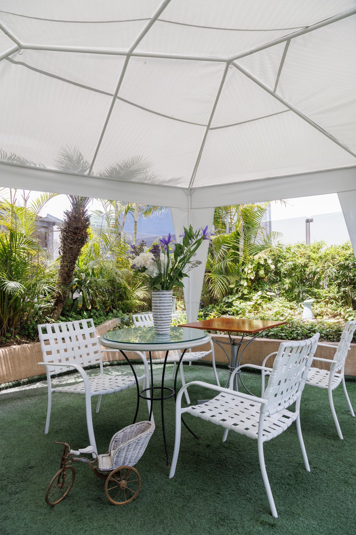 An outdoor patio with a round glass table, white wicker chairs, and a small bicycle.