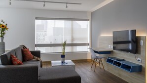 A modern living room with a sofa, a coffee table, a TV mounted on the wall, and a large window. - Daniel's Apart Hotel (Lima)