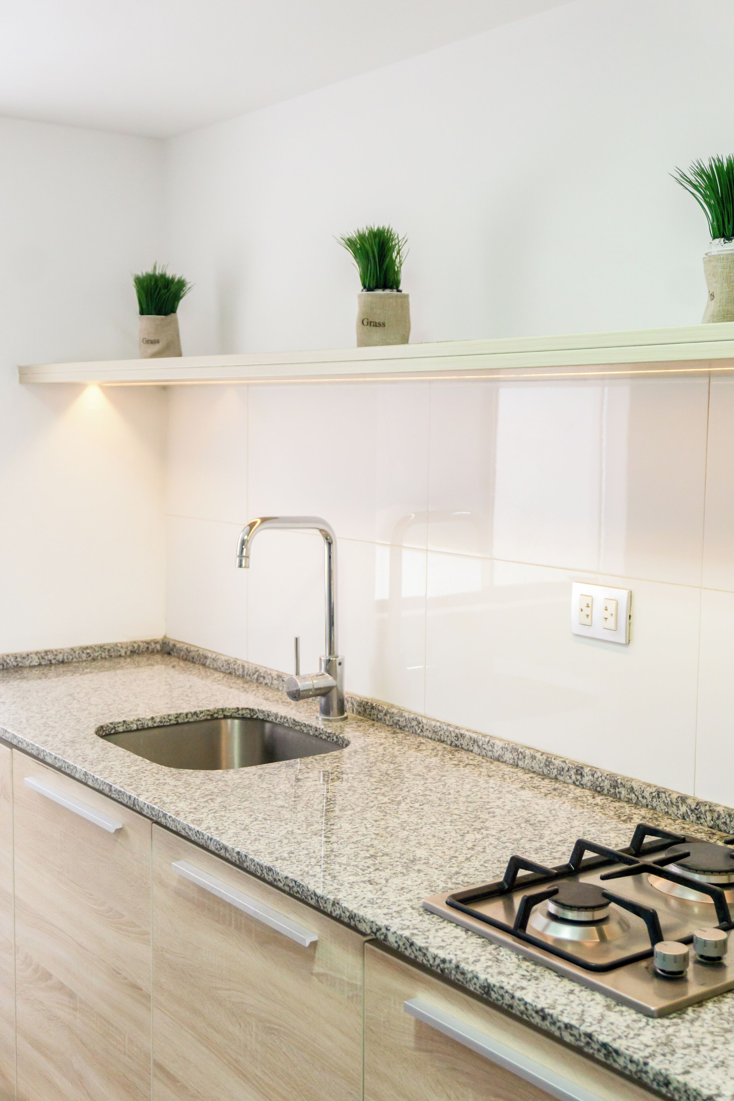 A modern kitchen with a granite countertop, stainless steel sink, and gas stove.