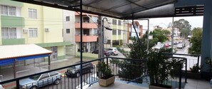 A balcony with a view of a street, a parked car, and a building with multiple floors and balconies. - Pousada Centralmar (Florianópolis)