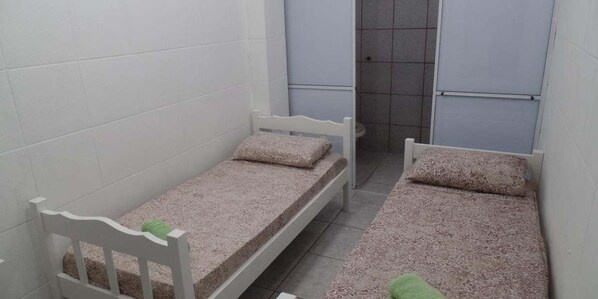 A small, narrow room with two single beds, each with a pillow and a blanket. - Pousada Centralmar (Florianópolis)