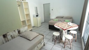 Una habitación pequeña y luminosa con una cama, una mesa con taburetes, un microondas y un armario.