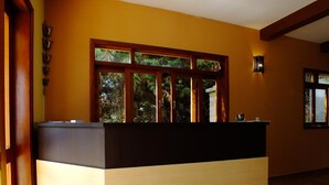 A reception desk with a dark and light wood finish, a window with a view of greenery, and a wall-mounted light fixture. - Pousada Vista da Serra (Camanducaia)