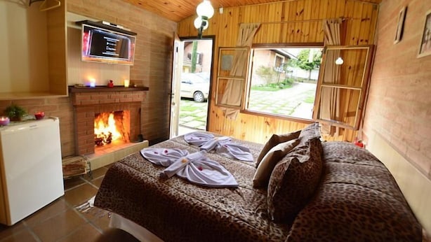 A cozy room with a fireplace, a bed with leopard print bedding, and a television mounted on the wall. - Pousada Aconchego (Camanducaia)