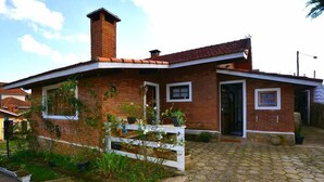 A single-story brick house with a tiled roof, a front porch with a white railing, and a paved driveway. - Pousada Aconchego (Camanducaia)