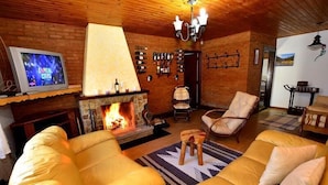 A cozy living room with a fireplace, leather sofas, a television, and a wine rack. - Pousada Aconchego (Camanducaia)