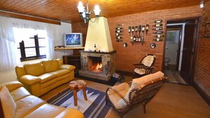 A cozy living room with a fireplace, a yellow sofa, a wicker chair, and a television. - Pousada Aconchego (Camanducaia)