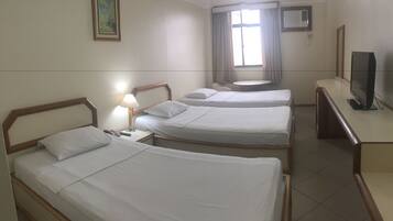 A hotel room with two single beds, a desk with a television, a window with curtains, and an air conditioning unit.
