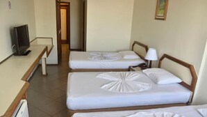 A hotel room with three single beds, a desk with a computer, and a door leading to another room. - Hotel Grão Pará (Belém)