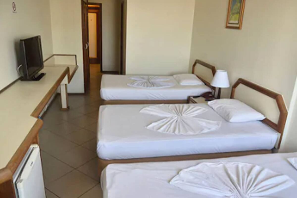 Habitación de hotel con tres camas individuales, un escritorio con computadora y una puerta que da a otra habitación.