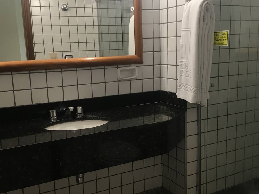Un baño con un lavabo negro, un espejo y una toalla blanca colgada en la pared.