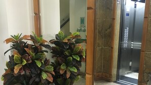 A hallway with two potted plants, a mirror reflecting an elevator, and a sign indicating a hotel. - Hotel Grão Pará (Belém)